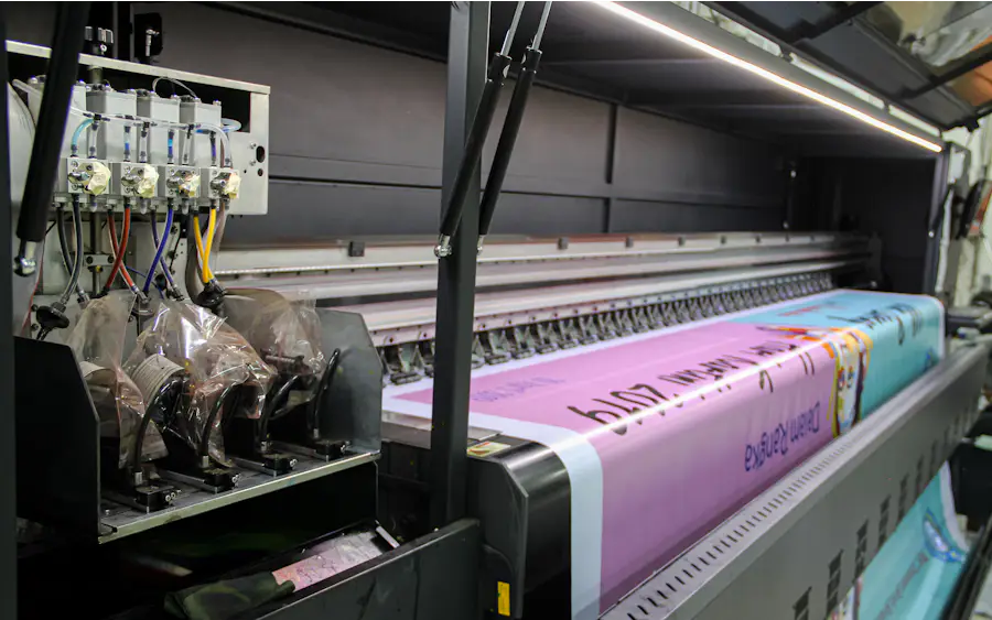 A wide-format press feeding a long printed banner through its rollers